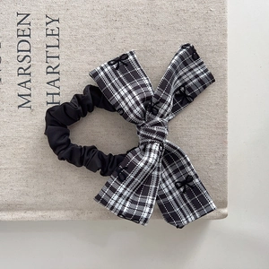 Close-up of black and white plaid scrunchie with embroidered bow detail on fabric