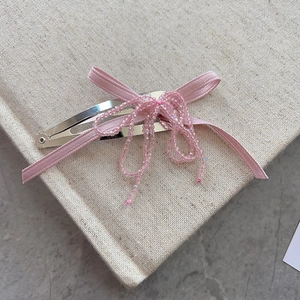Pink ribbon bow hair clip with crystal beaded tassels on a beige notebook background