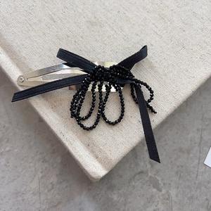 Elegant silver hair clip with black ribbon bow and beaded tassels on a vintage book