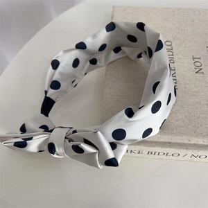 Detail of a beige polka dot headband with a bow placed on an artistic book on a desk