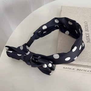 Close-up of a black satin polka dot headband with a bow and elastic comfort band