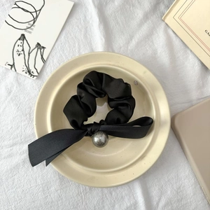 Detail eines schwarzen Satin-Haargummis mit langer Schleife und silberner Kugel