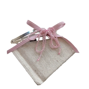 Elegant pink ribbon bow hair clip with beaded tassels on a rustic fabric background