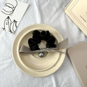 Detaillierte Nahaufnahme von schwarzem Seiden-Scrunchie mit grauer Schleife und Perle