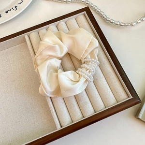 Detail of cream silk scrunchie with faux pearl charms on a soft jewelry display case