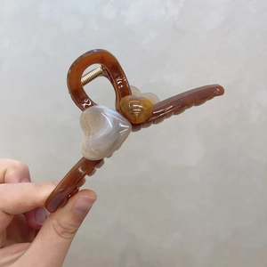 Détail de la pince à cheveux en résine ambrée avec double motif cœur et ressort métallique doré
