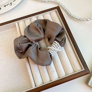 Brown satin scrunchie with layered pearl accent on a minimalist jewelry display tray