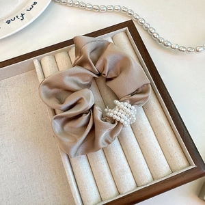 Elegant champagne satin scrunchie featuring five layers of pearls on a jewelry tray
