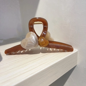 Détail de la pince à cheveux cœur ambre translucide avec ressort doré sur bois