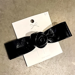 Close-up of black leather rose hair clip with bow design on a white display card