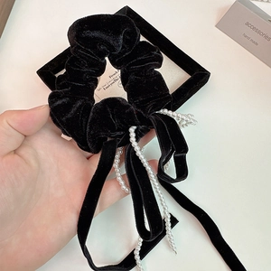Détail d'un chouchou en velours noir avec de longs rubans élégants et une chaîne de perles