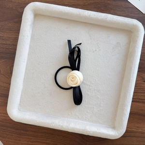 Detail view of cream fabric rose and black ribbon bow hair tie on a beige tray