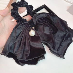 Détail d'un grand chouchou en velours noir avec un élégant pendentif en perle