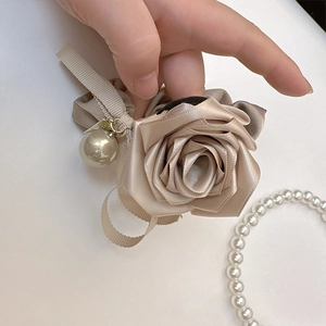Dettaglio di scrunchie rosa in raso champagne con perla crema e ciondolo dorato di lusso