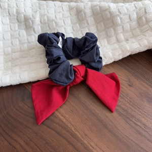 Navy blue ruffled scrunchie with red denim bow displayed on a rustic wooden table