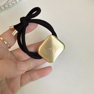 Close-up of golden brushed square metal piece on high-elasticity black hair tie rope