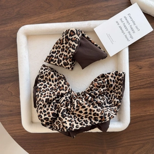 Close-up of leopard print hair scrunchie and bow set on white plush display tray