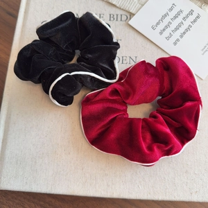 Detail of plush velvet hair scrunchies in black and burgundy with white piping finish