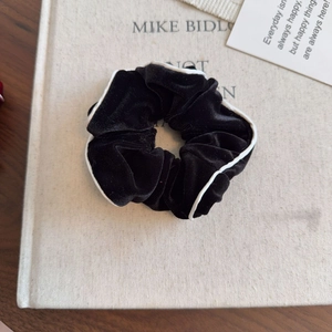 Elegant black velvet hair scrunchie with white trim edge on a cream book background