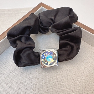 Close-up of black satin scrunchie featuring a large iridescent square crystal centerpiece