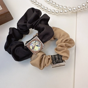 Detailed view of satin hair scrunchies with square crystal and woven tag on white background