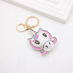 Cartoon unicorn PU leather keychain with gold hardware on a clean white desk background