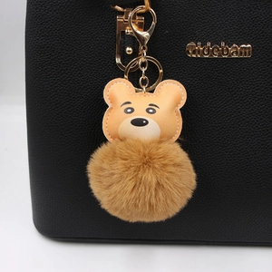 Cute brown tiger plush pom-pom keychain with leather details hanging on a black leather bag