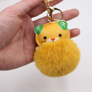 Handheld plush tiger keychain with vibrant yellow pom pom and gold metal hardware