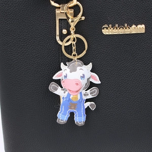 Porte-clés vache en cuir avec salopette bleue et clip doré sur un sac noir chic