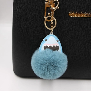 Blue shark pompom keychain with soft faux fur and gold metal hook on a black bag