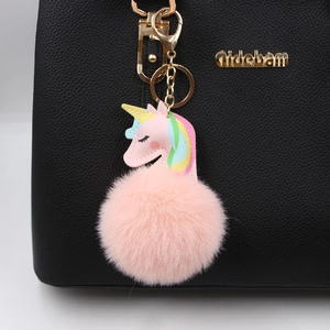 Pink faux fur unicorn keychain with golden hardware displayed on a black leather bag
