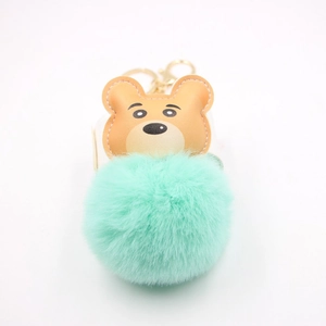 Close-up of a brown leather bear charm attached to a mint green fluffy pom pom keychain