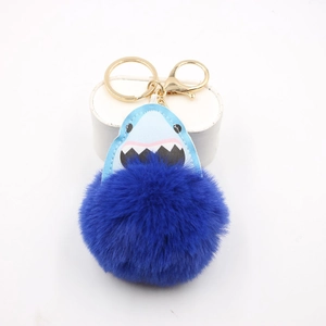 Detailed close-up of a blue shark plush pompom keychain with golden metal lobster clasp