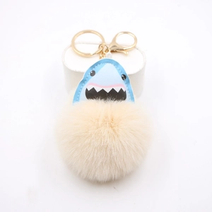 Close-up of fluffy apricot pompom keychain with blue leather shark detail and gold clip