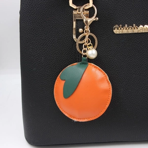Realistic persimmon fruit PU leather keychain with gold hardware on a black handbag