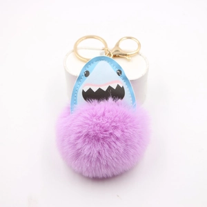 Detail of shark pom-pom keychain with purple faux fur and gold metal clasp on white stand