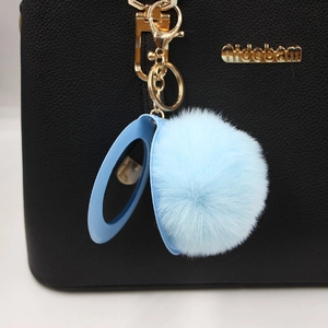 Blue faux fur pompom keychain with hidden vanity mirror on a black leather handbag