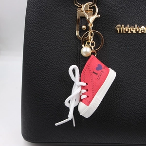 Portachiavi sneaker in tela rossa con cuore viola e clip dorata su borsa in pelle nera