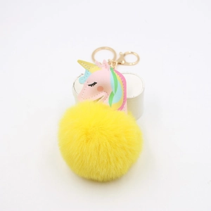 Detail of yellow fluffy pompom keychain with a cute pink unicorn and gold metal clip