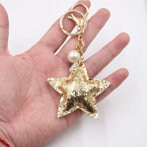 Glittering gold star keychain with faux pearl and spring clip accessory held by hand