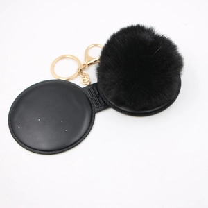 Detail view of black faux fur pompom keychain with golden metal clasp on white background