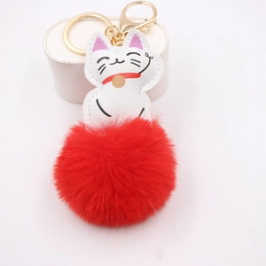 Lucky cat keychain with red pompom and gold lobster clasp on white display stand