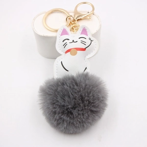 Detailed view of white lucky cat keychain with grey fluffy pompom and gold hardware