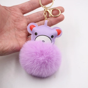 Handheld view of a cute purple leather bear charm with matching plush pom-pom and gold keychain