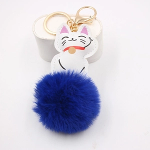 Close-up of fluffy royal blue pompom with a white Lucky Cat charm on a golden keychain