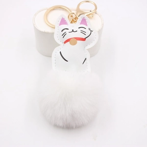 Detailed close-up of a white lucky cat keychain with a plush pompom and gold hardware