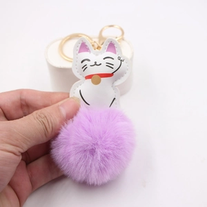 Detail of white lucky cat charm with purple pom-pom and gold metal keychain hook