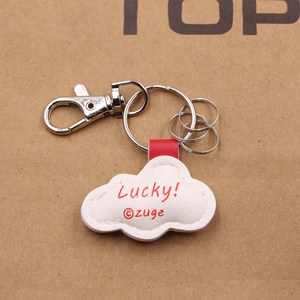 Detail eines weißen Wolken-Schlüsselanhängers aus Leder mit Lucky-Schriftzug und Haken