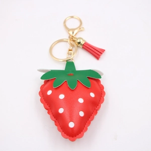 Close-up of strawberry faux leather keychain with red tassel and golden hardware detail
