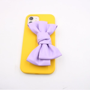 Detail of a bright yellow phone case featuring a large 3D light purple faux leather bow